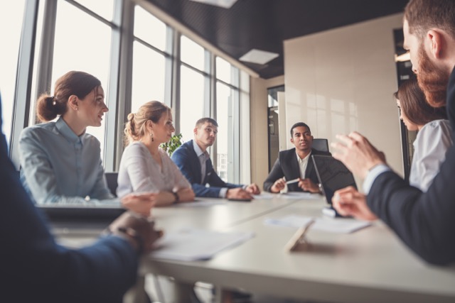 A diverse small team of professionals sit around a table strewn with laptops and papers, engaged in discussion
