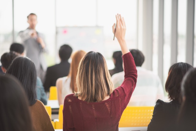 Woman raising up hand in a large group meeting