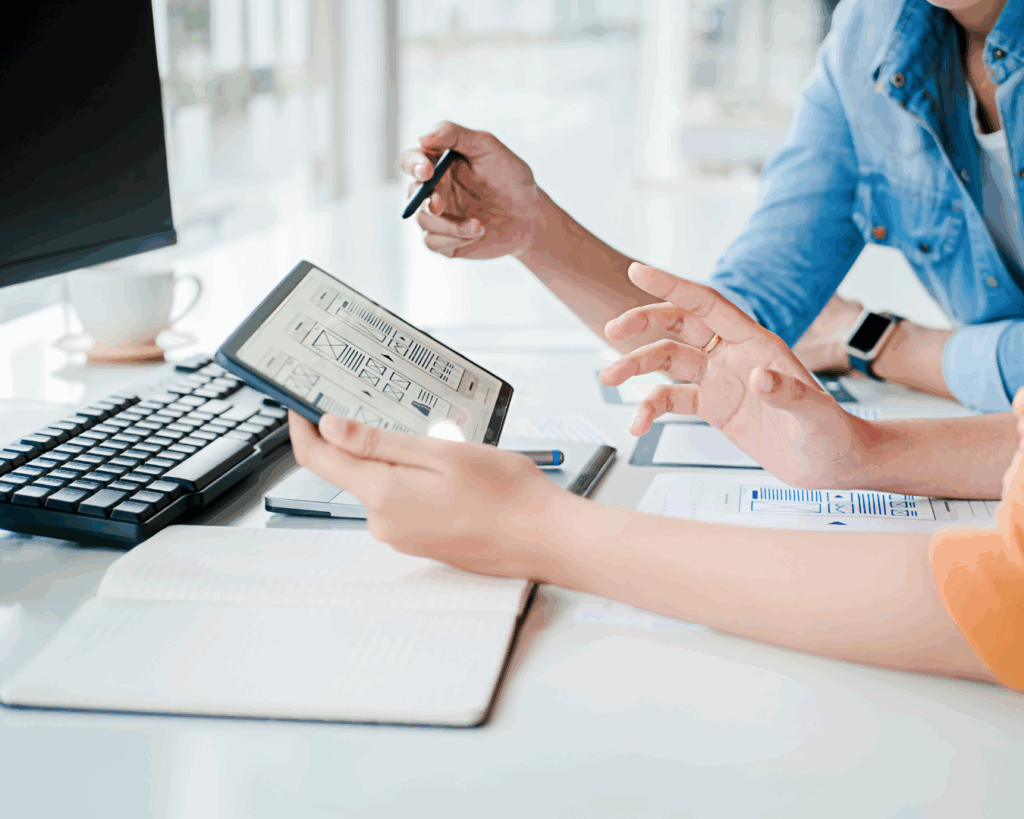 Photo of the hands of two web designers working together, discussing hand-drawn wireframes and UX sketches.